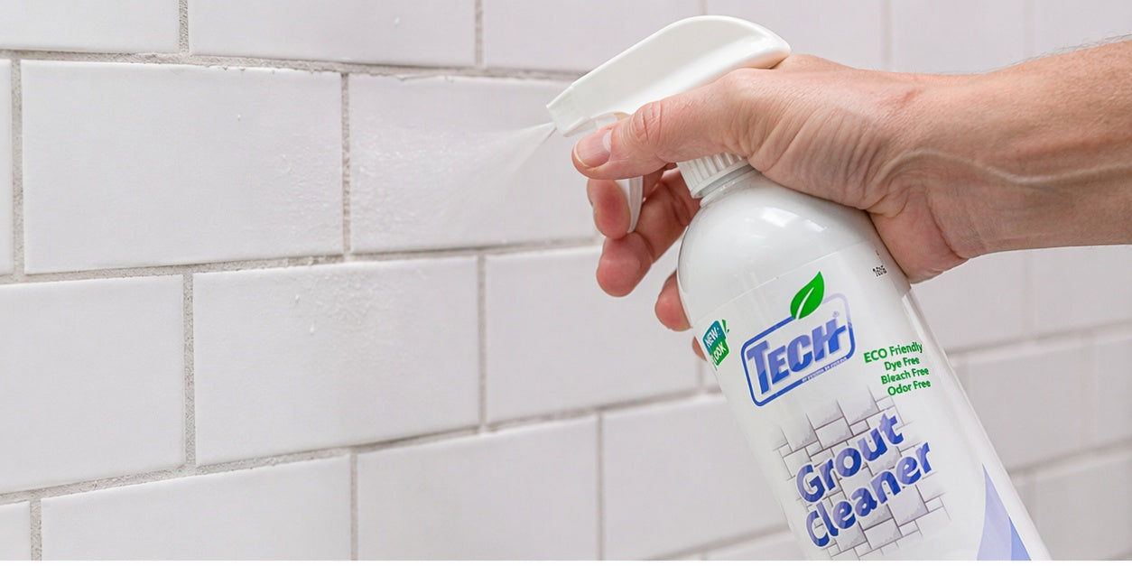Hand holding a bottle of TECH Grout Cleaner 24 oz against a tiled wall background